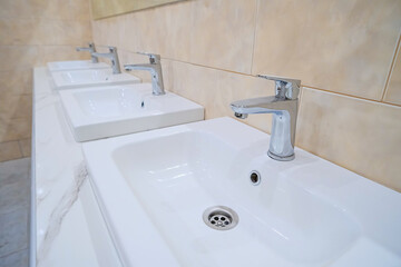 Fototapeta premium Several new and clean sinks with the same shiny chrome faucets are lined up in a row.