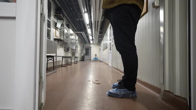Person wearing blue shoe covers stands in a clean hallway of a brewery, showcasing the sterile environment and preparation area