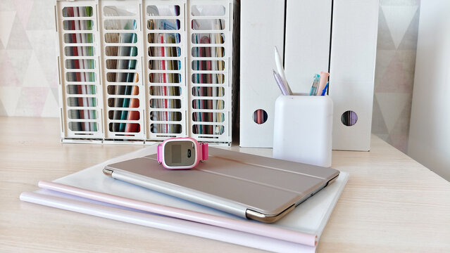 Smart watch for child lying on tablet computer on desk. Organized workspace with document storage and stationery. Modern home office or study interior concept for digital lifestyle.
