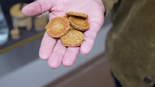 Hand holding several round, golden-brown beer snacks in a brewery setting, showcasing the texture and color of the treats
