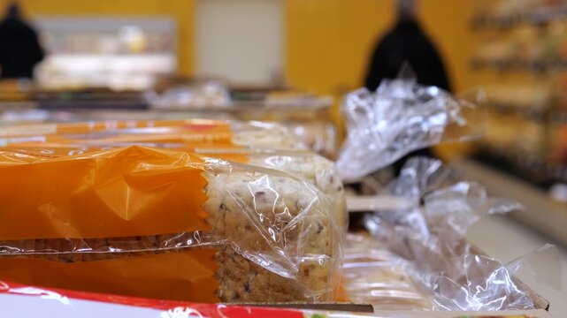 Close up of sliced bread in plastic packaging stacked on a grocery store shelf with unrecognizable shoppers walking in the blurred background, highlighting food retail and consumerism concepts