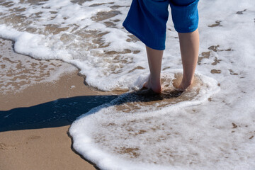 A refreshing wave of sea foam surrounds a person's feet on a sunny beach, captured in sharp detail. © Sergej