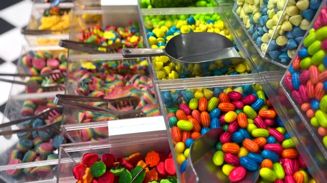 Wide variety of colorful candies, gummies, and bonbons displayed in clear plastic containers with serving scoops at a self serve pick and mix counter in a charming confectionary store