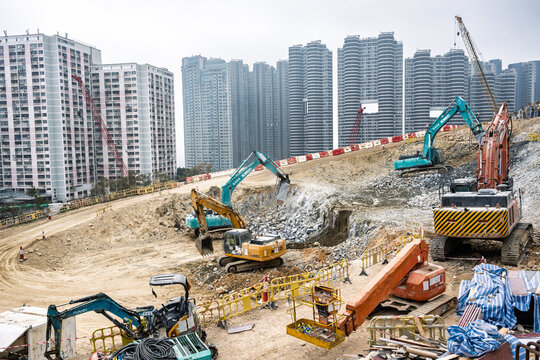 Hong Kong, Aberdeen, China, 2026: excavators working on large urban construction site below dense residential high rise buildings, showing rapid city development and infrastructure expansion