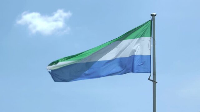 Sierra Leone flag waving in wind against blue sky, national symbol outdoor closeup