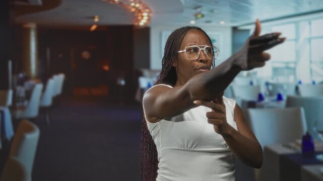 Young woman points finger like a gun and pulls her sleeve while standing in a restaurant building; determination resolve.