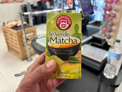Alicante, Spain - April 25, 2026: Hand holding Pompadour green tea with matcha box in a grocery store, visible checkout area and products in the background
