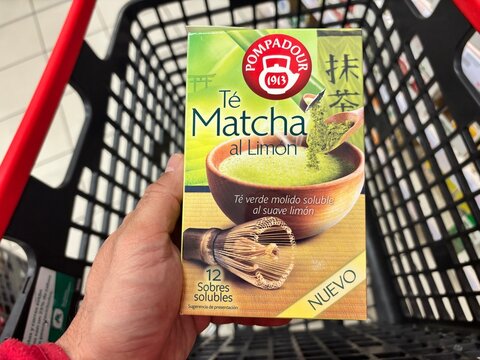 Alicante, Spain - April 25, 2026: Hand holding a box of Pompadour Matcha tea with lemon flavor inside a shopping cart in a grocery store