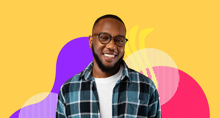 A young black man stands in front of a yellow studio background. He is smiling and wearing eyeglasses and a casual shirt. The scene shows joy and confidence in a playful setting. © Prostock-studio