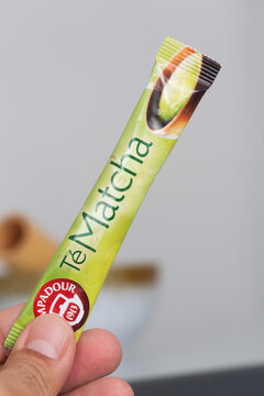Alicante, Spain - April 25, 2026: Matcha tea powder stick held in hand with visible branding and a blurred background of a bowl and cinnamon sticks