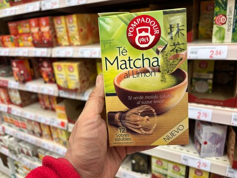 Alicante, Spain - April 25, 2026: Hand holding Pompadour Matcha tea box with lemon flavor in a grocery store aisle filled with various tea products