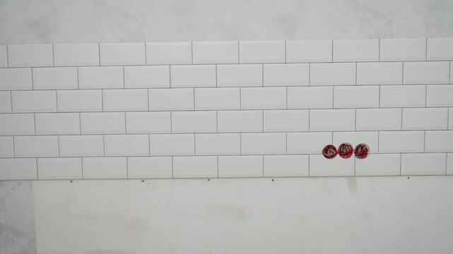 Panning shot across new white subway tile kitchen backsplash. Shows running bond pattern, electrical outlet cutouts, and corner detail. Concept of home renovation, remodeling, and interior design