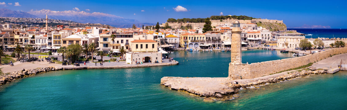 Breathtaking Rethymno Crete. Aerial 9K panorama. Spring view of Venetian lighthouse and old town with mosque against snowy Psiloritis mountains. Greece April travel scenery. Sea view coast 9000px