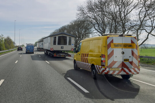 Netherlands, April 15, 2026. A yellow escort vehicle follows trucks carrying oversized prefabricated houses on a Dutch highway, marked with Transport Exceptionnel signs.