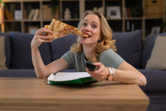 Woman enjoying pizza slice watching television at home