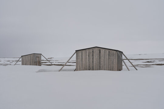 Svalbard, Svalbard and Jan Mayen - 21 June 2025: View of Kinnvika Station research huts braced against the wind in a snowy arctic landscape under a grey sky.