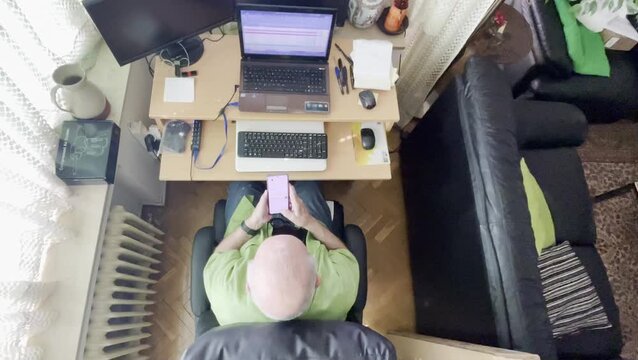 Abuelo jubilado usando tel&eacute;fono m&oacute;vil y ordenador port&aacute;til de pensionista activo con escritorio en perspectiva a&eacute;rea