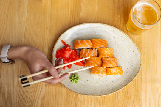 Salmon sushi rolls with beer. Top view of salmon sushi rolls with chopsticks, pickled ginger, wasabi, and a glass of beer on a wooden table.