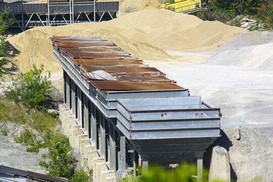 Metal aggregate bunkers beside sorted mounds of sand and crushed stone. Presents bulk construction sourcing, graded inert material staging, and calibrated feed management for infrastructure demand.