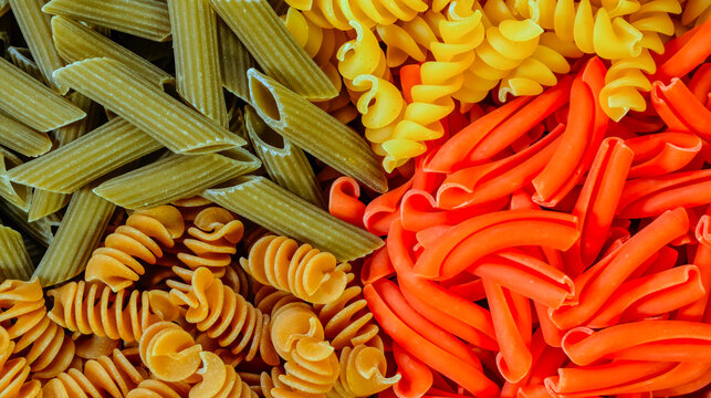 Assorted colorful dry pasta shapes including penne and fusilli