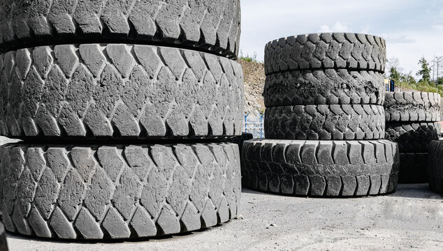 Close up large industrial tires stacked outdoors in gravel yard