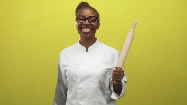 Young woman chef smiling holds rolling pin in right hand in studio while facing camera; joy confidence.