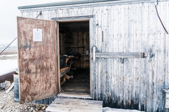 Svalbard, Svalbard and Jan Mayen - 21 June 2025: View of Kinnvika Station, a historic research base with a weathered wooden shack and open rusty door in the arctic landscape.