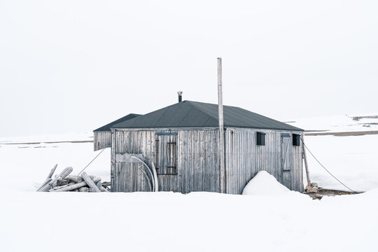 Svalbard, Svalbard and Jan Mayen - 21 June 2025: View of Kinnvika Station with its weathered wooden buildings surrounded by a vast snowy landscape under a white overcast sky.