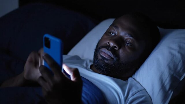 A surprised man in bed reacts to something on his phone.