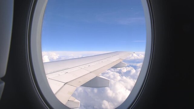Looking out airplane illuminator at cloudy landscape outside window during flight
