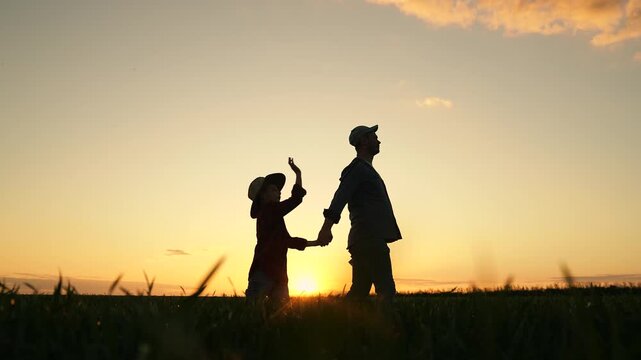 Father child walk on field, sky sunrise. Kid boy, dad go hand in hand, field corn sprouts. Dad child son hold hands in field. Family farming business. Agricultural industry. Growing corn, organic food