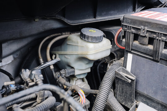 Car brake fluid reservoir inside engine bay. Automotive maintenance detail. Vehicle service inspection scene. Plastic coolant tank and battery compartment closeup. Repair workshop concept.