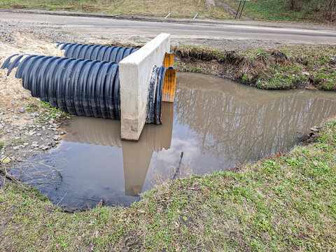 Culvert system under road with muddy water reflection and concrete headwall along the roadside