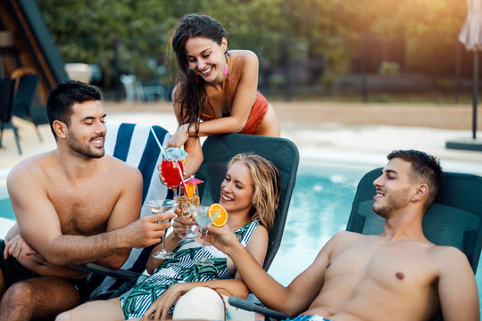 Group of friends enjoy drinks together by a pool on a sunny day during summer vacation