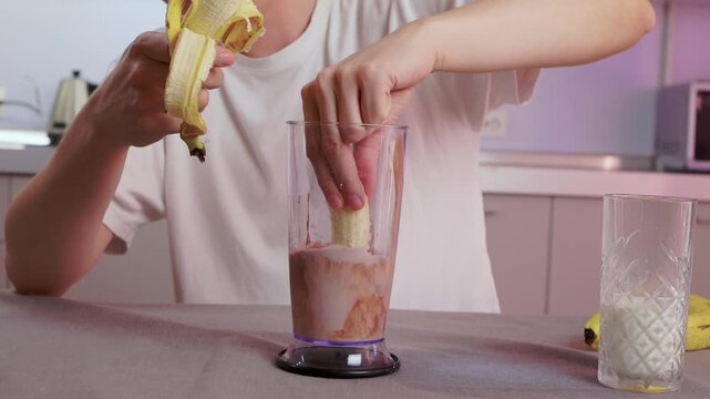 Casual kitchen smoothie preparation. Banana being mashed into chocolate beverage in kitchen. Person preparing chocolate banana smoothie on modern kitchen counter