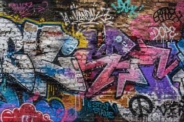 Obraz premium A colorful urban graffiti wall fills the frame with layered spray paint letters symbols and rough texture creating a vibrant street art background for youth culture and city expression