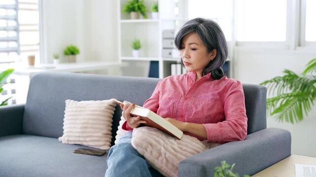 Senior Asian woman suffering eye strain while reading book at home  Elderly lifestyle concept, vision problem, stress and health issue.