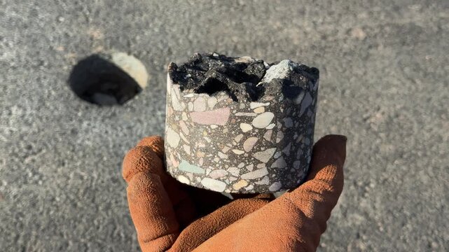 worker holding an asphalt core sample taken from a road surface, with a drilled hole visible