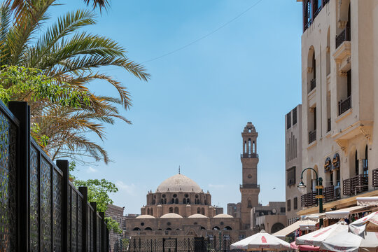 El-Darb El-Ahmar, Egypt - 20 April 2026: View of Abu Dahab Mosque with its stone dome and minaret under a clear blue sky, framed by palm trees and urban buildings.