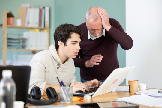 Young and elderly men sit together at laptops, sad and tense, solving work problems or facing difficult situation in office