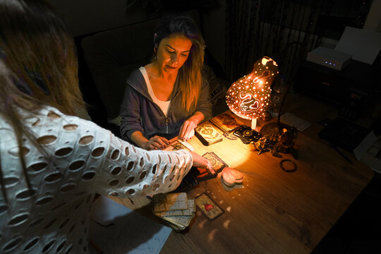 Focused woman interpreter reading tarot cards with mystical gourd lamp at night