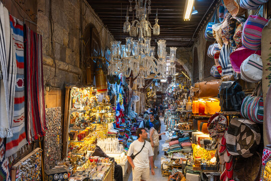 Cairo, Egypt - 20 April 2026: View of Khan el-Khalili bazaar with people walking past shops filled with traditional lamps, textiles, and leather goods under hanging chandeliers.