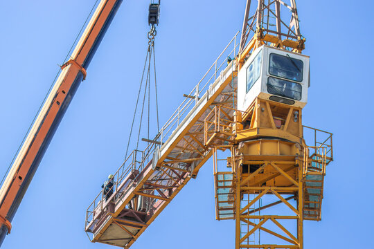 Construction crane with operator in cabin, lifting materials against clear blue sky, showcasing industrial machinery and construction site environment