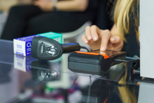 Female cashier using a payment terminal while scanning items with a barcode scanner at a retail store checkout counter with products visible in the background