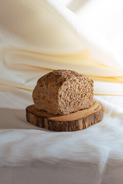 Rustic whole grain bread on wooden board with soft fabric background