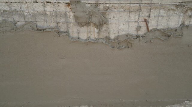 Close up shot of fresh wet plaster being applied to a concrete wall with reinforcing wire mesh. Construction or renovation in progress. Shows texture of materials like cement and metal