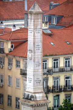 Lisboa, Portugal - 7 April 2026: View of the Monument to the Restorers obelisk with its detailed inscriptions against a backdrop of traditional red-tiled rooftops and yellow buildings.