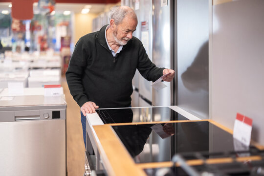 Elderly man buyer chooses electric stove in home appliance store