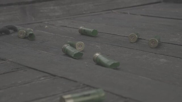 Discarded ammunition shells spread over textured outdoor wooden planks. Collection of used shotgun cartridges rests on weathered wooden decking with detailed chains nearby