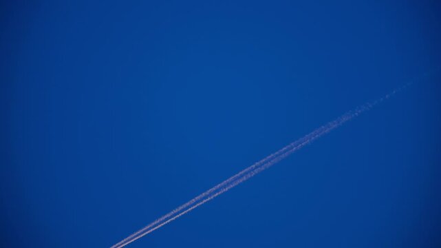 High Altitude Aircraft Leaving Vapor Trail in Sky. Airplane Crossing Blue Sky with Long White Trail. Jet Stream Trail Behind Airplane in Clear Sky. Minimal Sky Scene Plane and Contrail Motion. 